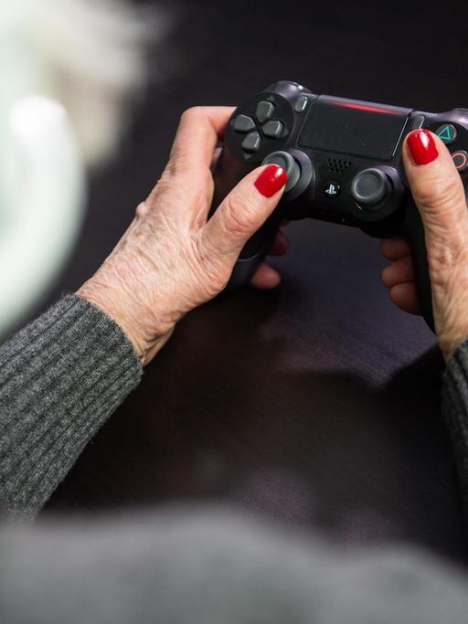 Eine Seniorin hält den Controller einer Playstation in den Händen.