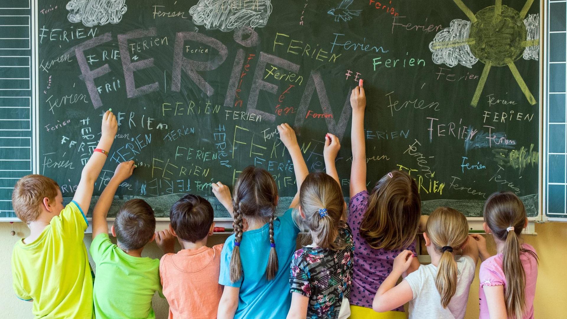 Kinder einer Grundschule schreiben das Wort Ferien an eine Tafel