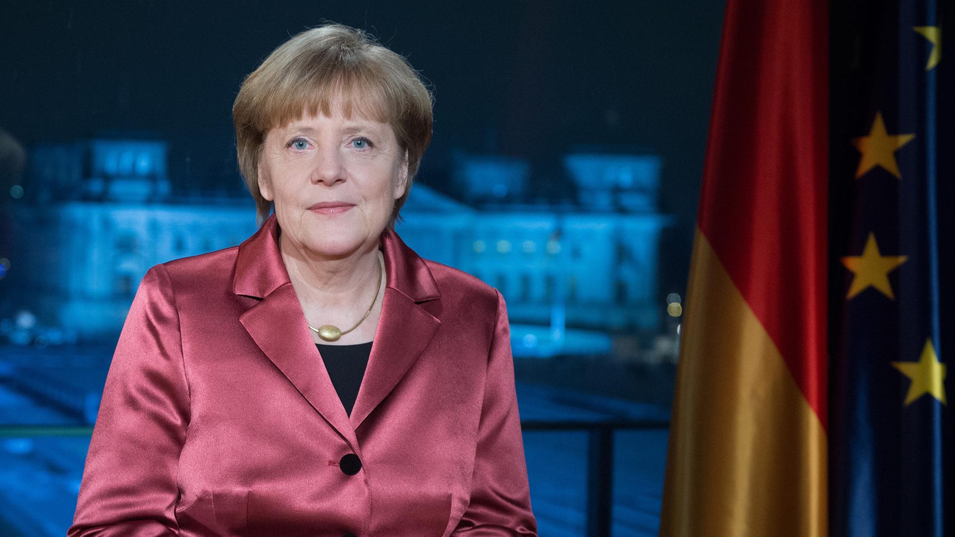 Angela Merkel an einem Schreibtisch vor Deutschland- und EU-Flagge, im Hintergrund der Blick durchs Fenster auf den Reichstag. Angela Merkel an einem Schreibtisch vor Deutschland- und EU-Flagge, im Hintergrund der Blick durchs Fenster auf den Reichstag.