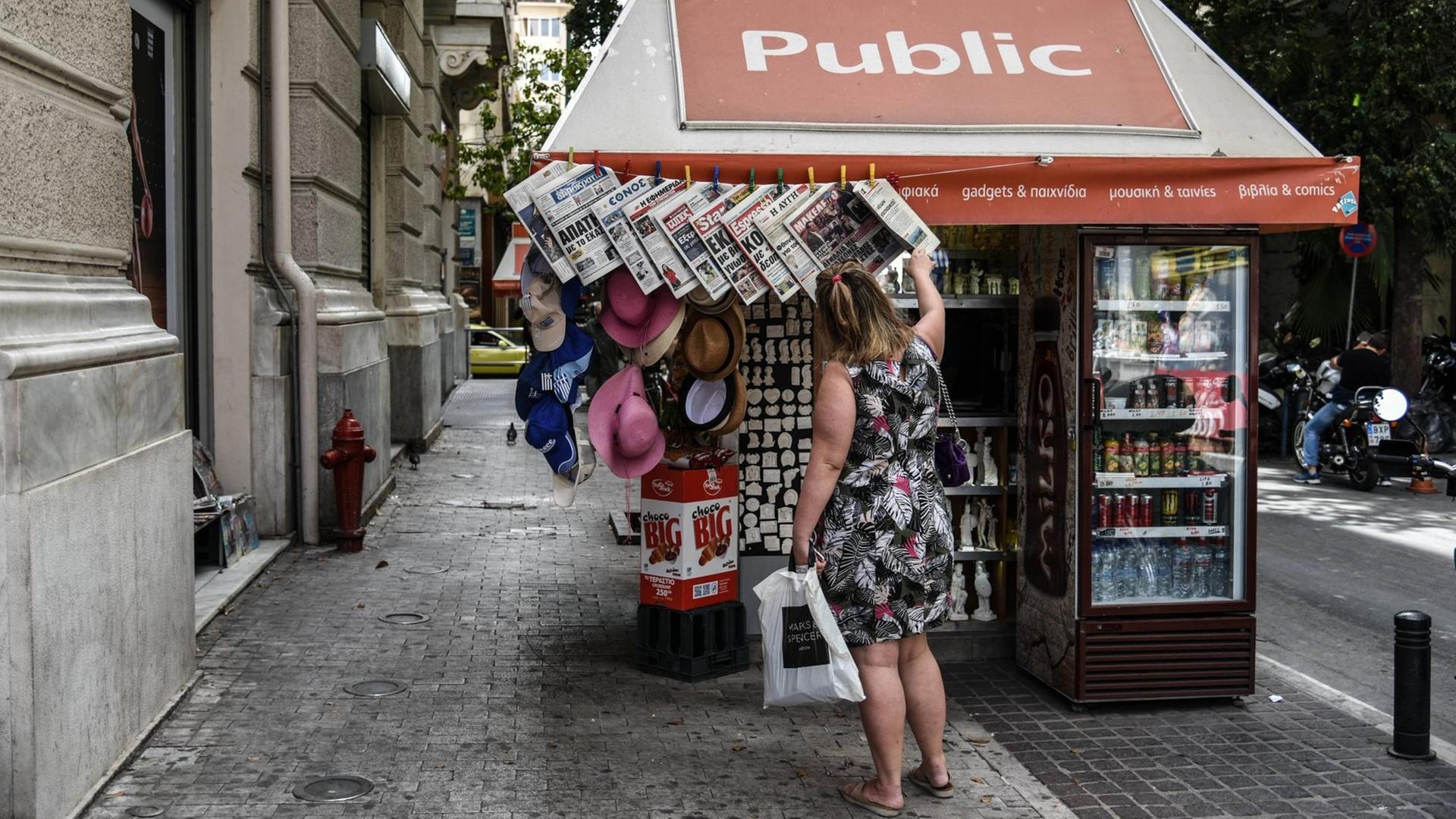 Eine Frau schaut sich die Titelseiten der Zeitungen an einem Kiosk in Athen an. Eine Frau schaut sich die Titelseiten der Zeitungen an einem Kiosk in Athen an.