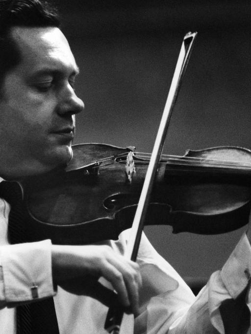 Schwarz-Weiß Foto: Ein Mann mit dunklen zurückgekämmten Haaren spielt Geige. Er trägt weißes Hemd und dunklen Schlips.