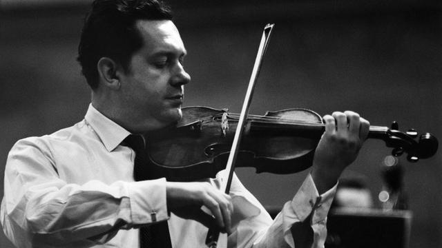 Schwarz-Weiß Foto: Ein Mann mit dunklen zurückgekämmten Haaren spielt Geige. Er trägt weißes Hemd und dunklen Schlips.