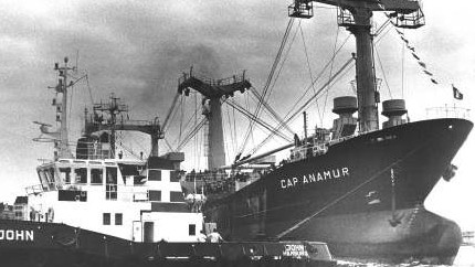 Das Schwarz-Weiß-Bild zeigt die Cap Anamur neben einem Schlepper. Das Schwarz-Weiß-Bild zeigt die Cap Anamur neben einem Schlepper.
