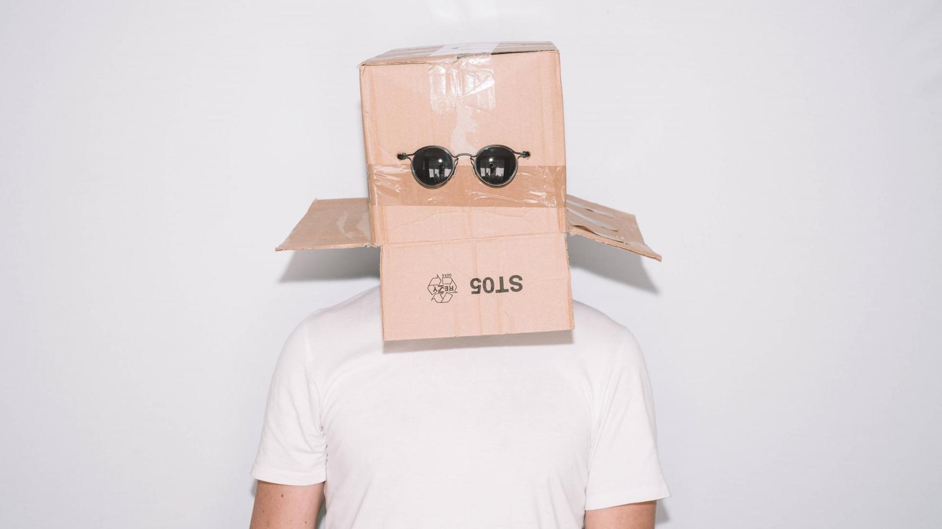 Ein Mann in weißem T-Shirt hat sich einen Pappkarton übergestülpt, an dem auf Augenhöhe eine Sonnenbrille befestigt ist. Ein Mann in weißem T-Shirt hat sich einen Pappkarton übergestülpt, an dem auf Augenhöhe eine Sonnenbrille befestigt ist.