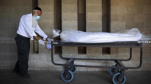 Ein Mitarbeiter der "Hevra Kadisha", Israels öffizieller jüdischer Bestattungsgesellschaft, transportiert eine Leiche auf einem Rollwagen. Er trägt einen Mund-Nasen-Schutz.