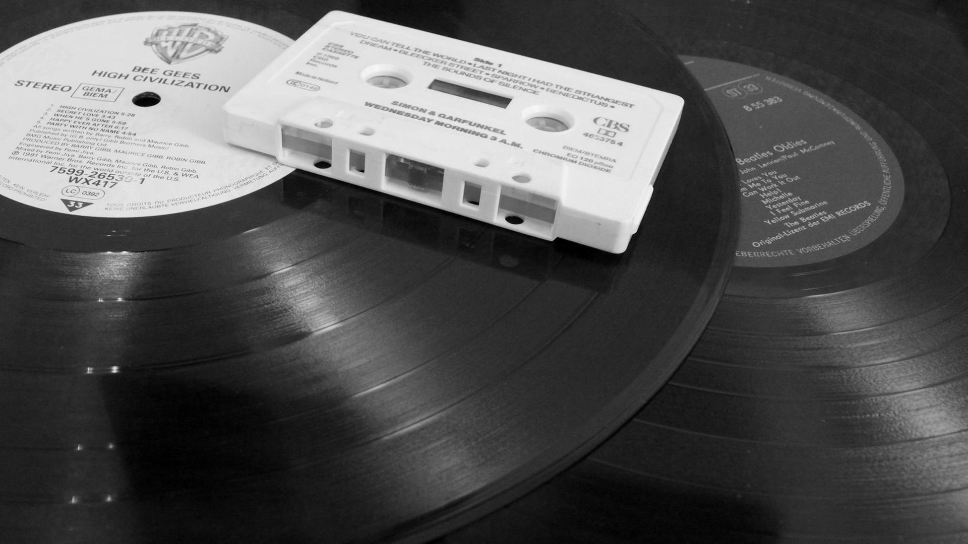 ILLUSTRATION - Eine Audio-Kompaktkassette (Musikkassette, MC, Audiokassette) liegt am 12.12.2014 in Berlin auf zwei Vinyl-Schallplatten (Langspielplatten, LP). Die mit einem Magnetband ausgerüstete Kassette, die in den 1970er Jahren bis in die 1990er Jahre hinein weit verbreitet war, wurde in einem Kassettenrekorder abgespielt und ermöglichte erstmals den mobilen Konsum von Musik. Beide Tonträger haben mit der Einführung der digitalen Audiotechnik der CD (Kompaktdisc) an Bedeutung verloren. Foto: Peter Zimmermann | Verwendung weltweit ILLUSTRATION - Eine Audio-Kompaktkassette (Musikkassette, MC, Audiokassette) liegt am 12.12.2014 in Berlin auf zwei Vinyl-Schallplatten (Langspielplatten, LP). Die mit einem Magnetband ausgerüstete Kassette, die in den 1970er Jahren bis in die 1990er Jahre hinein weit verbreitet war, wurde in einem Kassettenrekorder abgespielt und ermöglichte erstmals den mobilen Konsum von Musik. Beide Tonträger haben mit der Einführung der digitalen Audiotechnik der CD (Kompaktdisc) an Bedeutung verloren. Foto: Peter Zimmermann | Verwendung weltweit