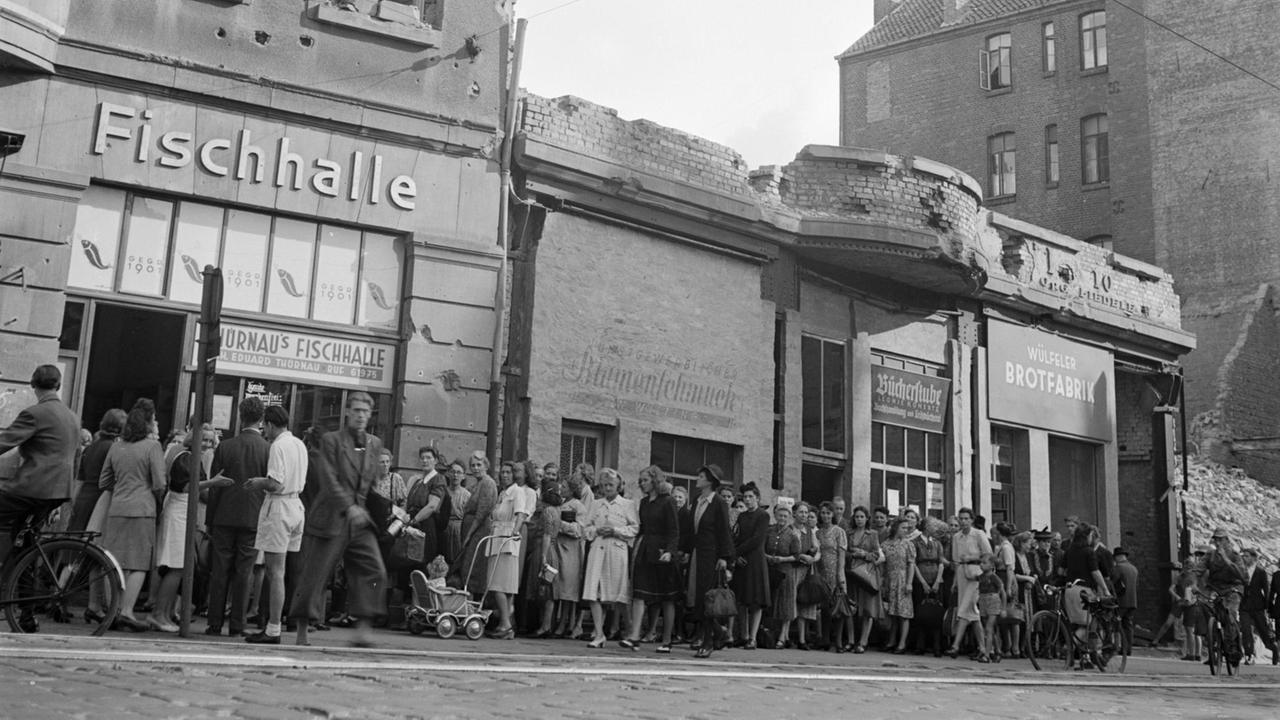 Eine historische schwarz-weiß Aufnahme von 1947 zeigt eine lange Warteschlange vor Thürnaus Fischhalle in Hannover. Die Straße und die Gebäude sind noch vom Bombenkrieg schwer gezeichnet.