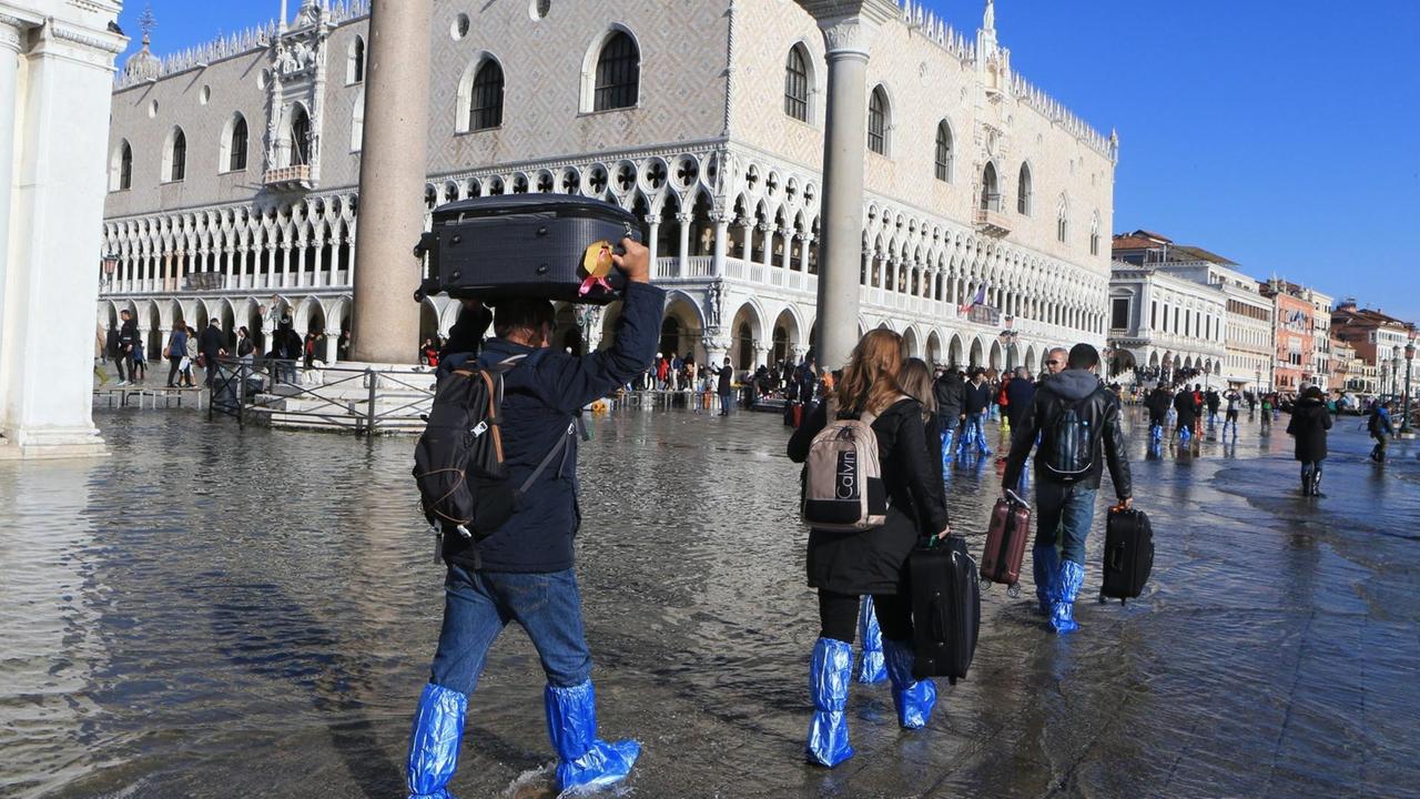 Venedig leidett im November 2019 unter einem der schlimmsten Überschwemmung nach Starkregen. Das Foto zeigt Leutein Gummistiefeln und Schutzmanschetten, die ihre Taschen teils über dem Kopf tragen.