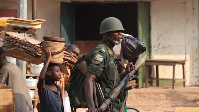 Ein bewaffneter Soldat steht auf einer Straße, um ihn herum Zivilisten.