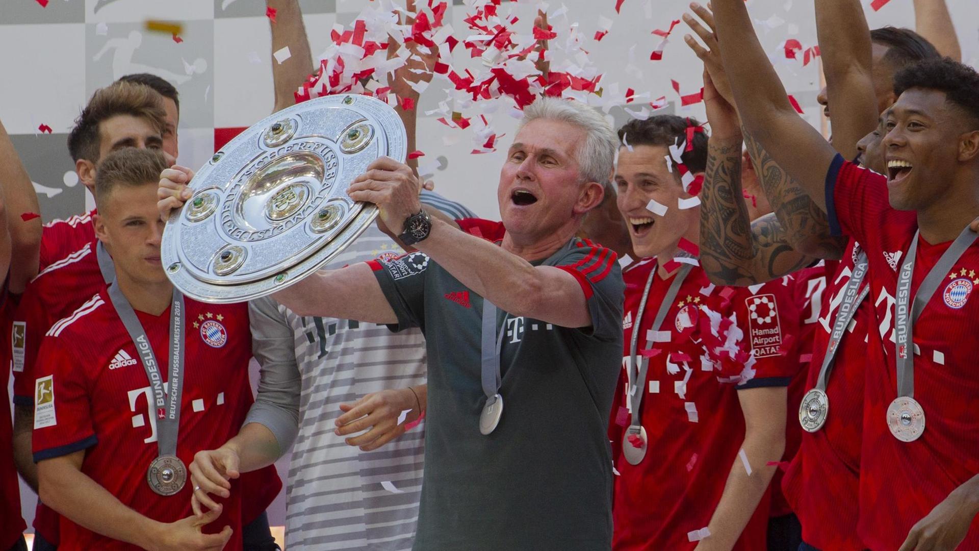 Jupp Heynckes steht zwischen den Spielern Joshua Kimmich, Sebastian Rudy und David Alaba und hält die Meisterschale hoch, die der Verein in der Saison 2017/18 gewonnen hat. Im Hintergrund rieseln rote und weiße Papierfetzen herab, die Farben des Klubs. Jupp Heynckes steht zwischen den Spielern Joshua Kimmich, Sebastian Rudy und David Alaba und hält die Meisterschale hoch, die der Verein in der Saison 2017/18 gewonnen hat. Im Hintergrund rieseln rote und weiße Papierfetzen herab, die Farben des Klubs.