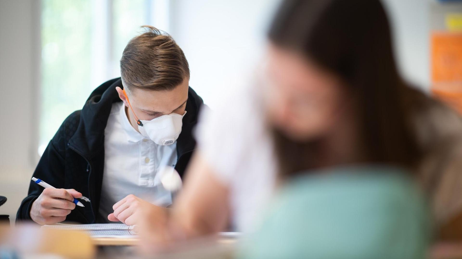 Schülerinnen und Schüler, einer davon mit einer Schutzmaske, bearbeiten Informatikaufgaben. Schülerinnen und Schüler, einer davon mit einer Schutzmaske, bearbeiten Informatikaufgaben.