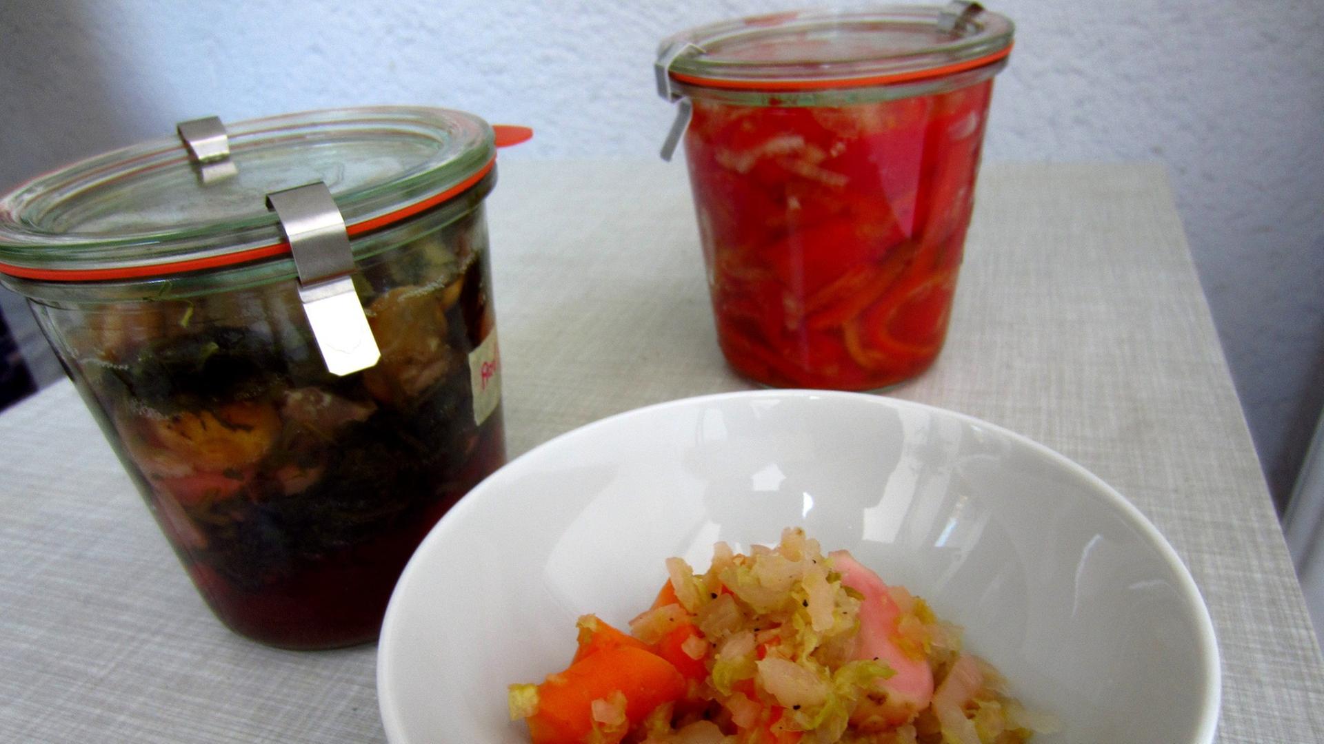 Eingelegtes Gemüse in Einmachgläsern neben Sauerkraut in einer Schale Eingelegtes Gemüse in Einmachgläsern neben Sauerkraut in einer Schale