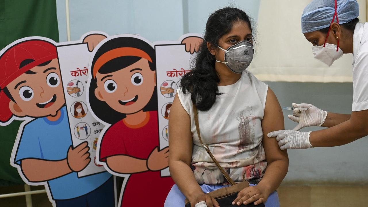 Eine jüngere Frau wird in einem indischen Krankenhaus geimpft, hinter ihr stehen Schautafeln mit Hygieneregeln. Eine jüngere Frau wird in einem indischen Krankenhaus geimpft, hinter ihr stehen Schautafeln mit Hygieneregeln.