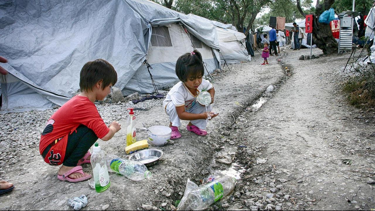 Zwei Flüchtlingskinder im Zeltlager beim Abwasch mit Wasserflaschen Zwei Flüchtlingskinder im Zeltlager beim Abwasch mit Wasserflaschen