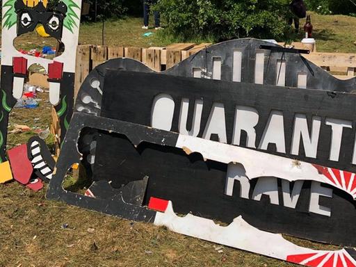 Auf einem Schild steht der Schriftzug "Quarantine Rave", daneben ist viel Müll zu sehen.