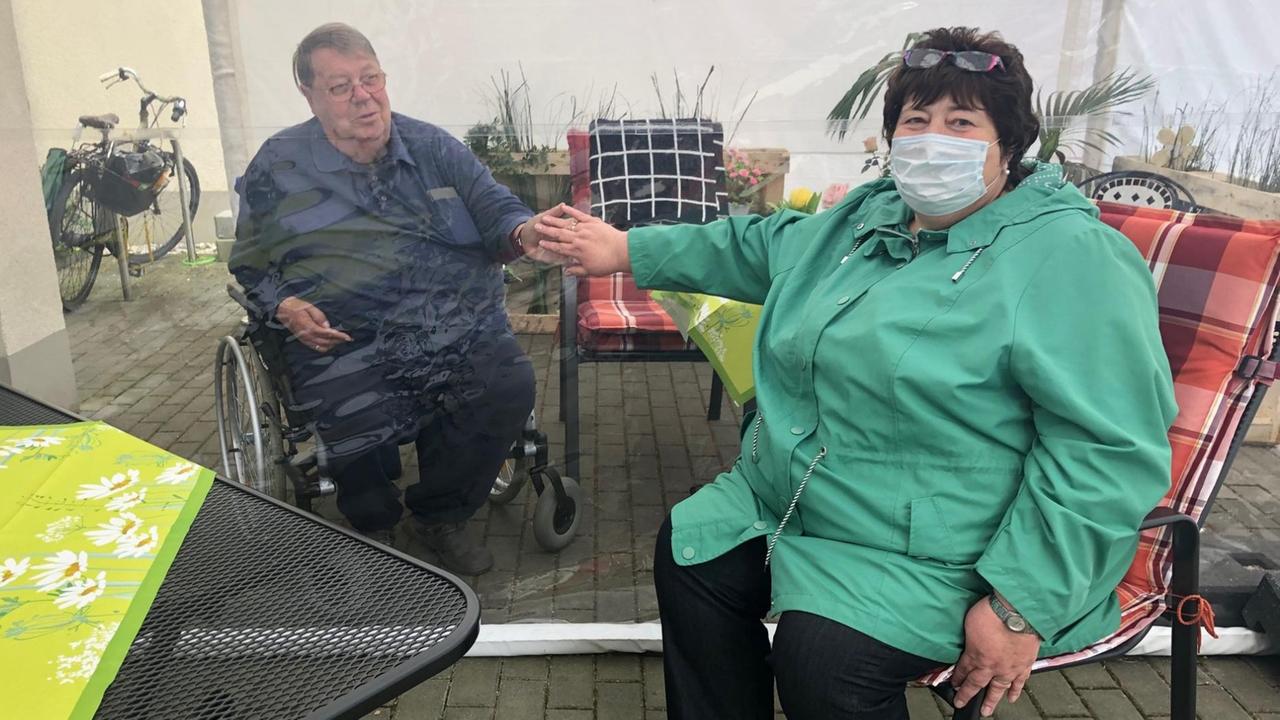 Heimbewohner Karl Josef Gegner reicht seiner Freundin Ilona Spottke im Begegnungszelt die Hand. Sie trennt ein Plastikvorhang. Heimbewohner Karl Josef Gegner reicht seiner Freundin Ilona Spottke im Begegnungszelt die Hand. Sie trennt ein Plastikvorhang.