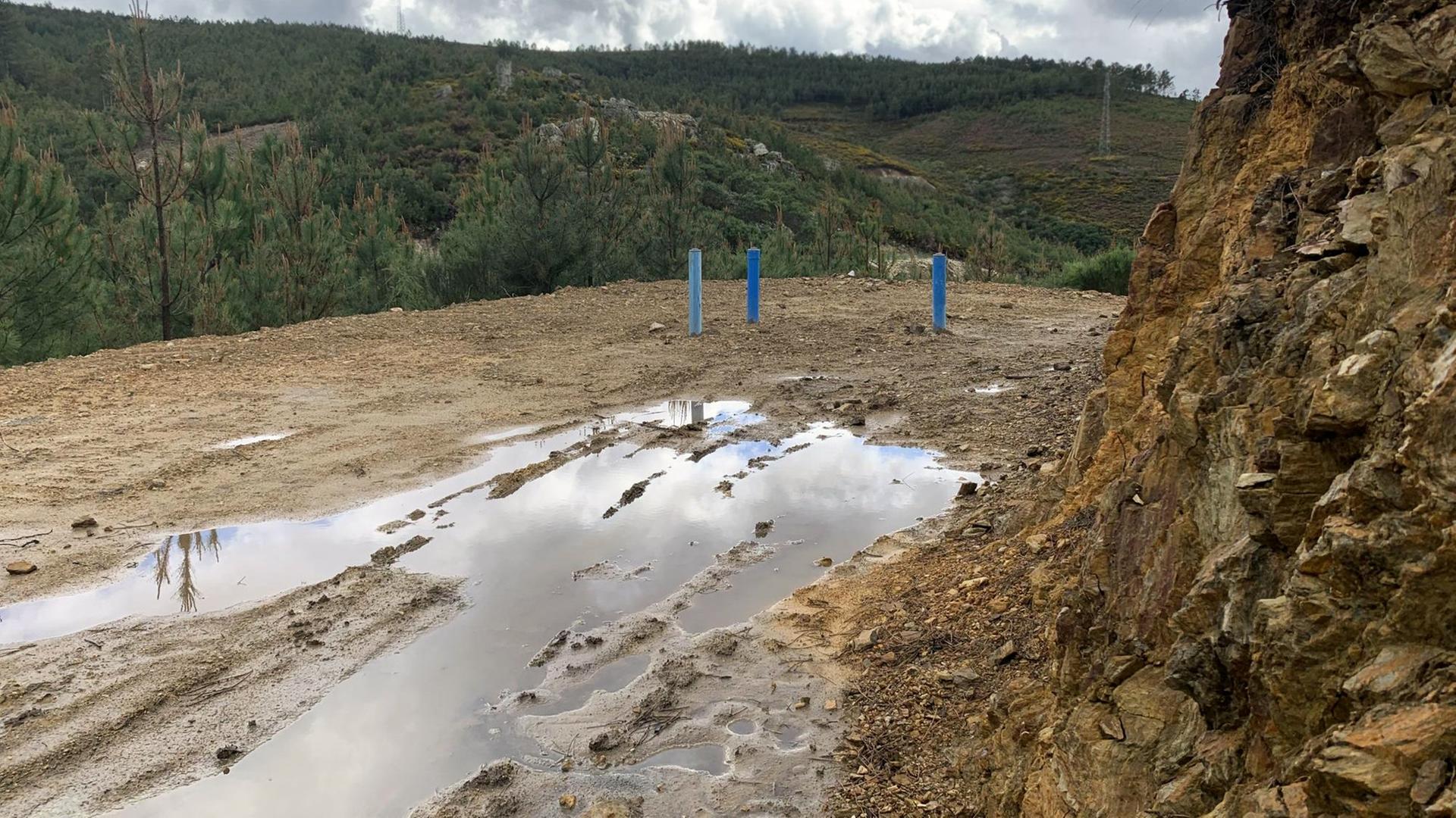 Ein steiniger Abhang, davor Wasserlachen auf einem breiten erdigen Weg. Im Hintergrund bewaldete Hügel. Ein steiniger Abhang, davor Wasserlachen auf einem breiten erdigen Weg. Im Hintergrund bewaldete Hügel.