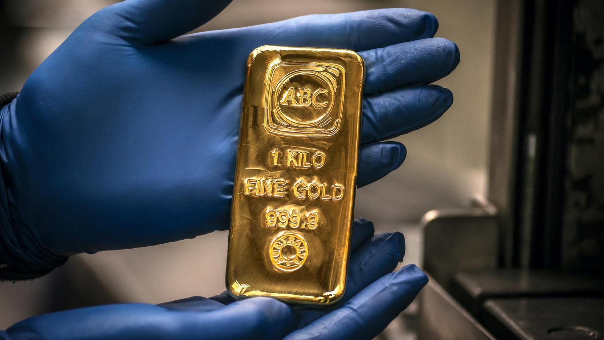 Ein Arbeiter hält einen Ein-Kilogramm-Goldbarren in den Händen. Ein Arbeiter hält einen Ein-Kilogramm-Goldbarren in den Händen.