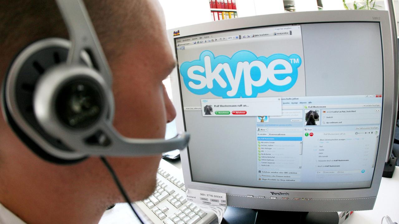 Ein junger Mann sitzt mit einem Headset vor einem Computerbildschirm und nutzt Skype.