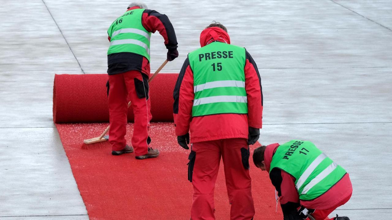 Drei Arbeiter in grünen Warnwesten mit der Aufschrift "Presse" arbeiten an dem fast komplett aufgerollten Teppich. Einer fegt Schneegraupel weg. Drei Arbeiter in grünen Warnwesten mit der Aufschrift "Presse" arbeiten an dem fast komplett aufgerollten Teppich. Einer fegt Schneegraupel weg.