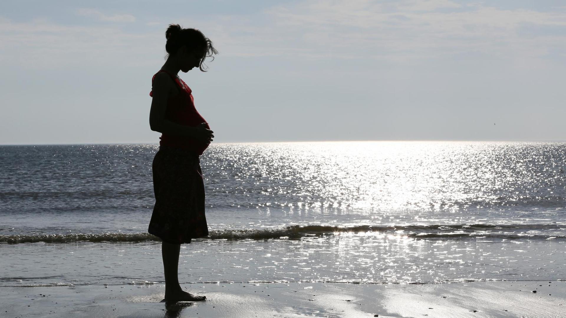 Eine im neunten Monat schwangere Frau steht am Strand von St. Peter Ording. Eine im neunten Monat schwangere Frau steht am Strand von St. Peter Ording.