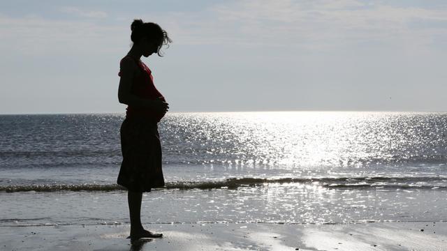 Eine im neunten Monat schwangere Frau steht am Strand von St. Peter Ording.