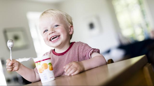  Ein zweijähriger Junge isst einen Fruchtjoghurt. 
