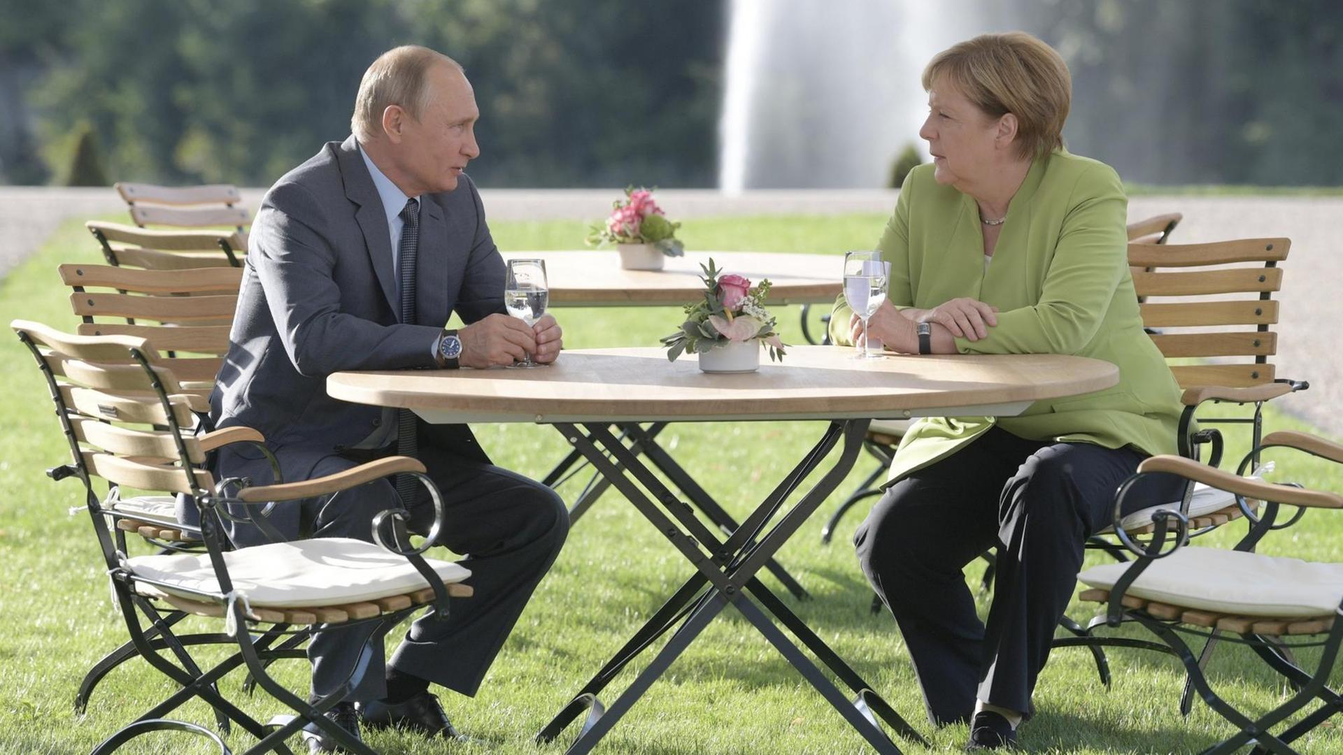 Merkel und Putin sitzen auf Gartenstühlen im Park von Schloss Meseberg.