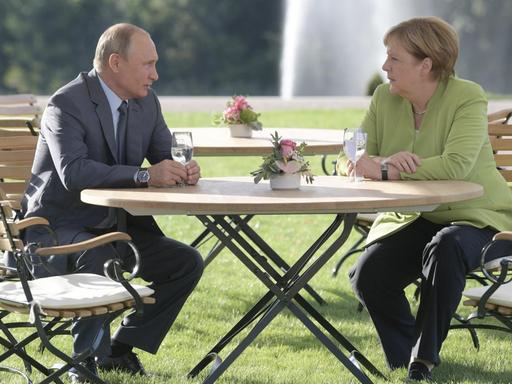 Merkel und Putin sitzen auf Gartenstühlen im Park von Schloss Meseberg.