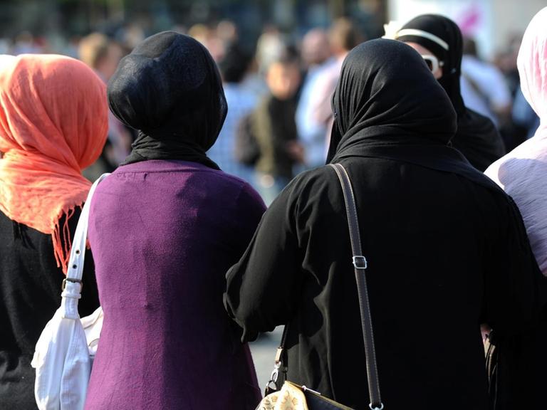 Fünf Frauen mit Kopftüchern, von hinten fotografiert. 