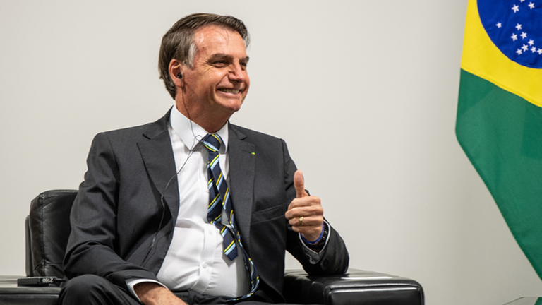 Jair Bolsonaro sitzt neben einer Flagge Brasiliens. Jair Bolsonaro sitzt neben einer Flagge Brasiliens.