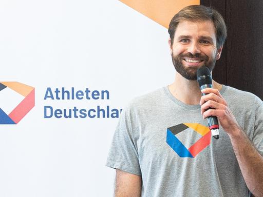 Johannes Herber spricht bei einer Veranstaltung freundlich lachend in ein Mikrofon. Johannes Herber spricht bei einer Veranstaltung freundlich lachend in ein Mikrofon.