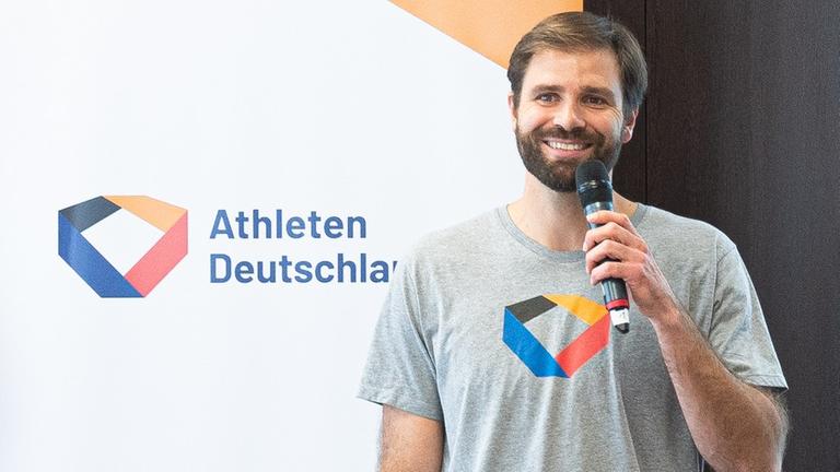 Johannes Herber spricht bei einer Veranstaltung freundlich lachend in ein Mikrofon. Johannes Herber spricht bei einer Veranstaltung freundlich lachend in ein Mikrofon.