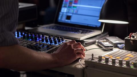 Ein Soundkünstler arbeitet mit Mischpult und Computer.