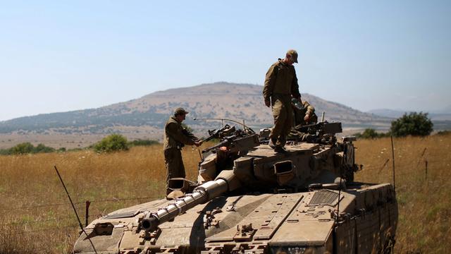 Mehrere Soldaten stehen auf einem Panzer, der inmitten von verdorrtem Gras steht, im Hintergrund ein Hügel