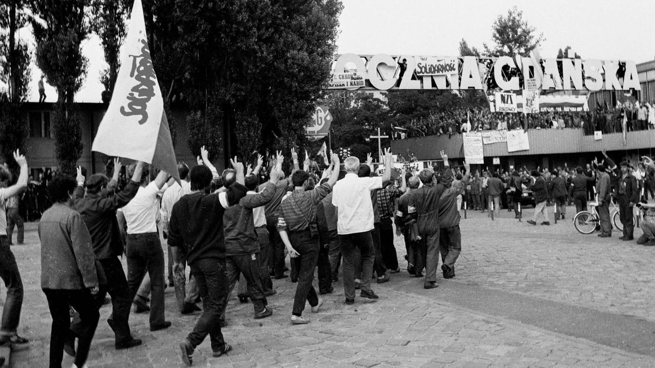Streikende Arbeiter laufen mit geschwenkten Solidarność-Fahnen durch das Werktor der Lenin Werft in Danzig. Streikende Arbeiter laufen mit geschwenkten Solidarność-Fahnen durch das Werktor der Lenin Werft in Danzig.