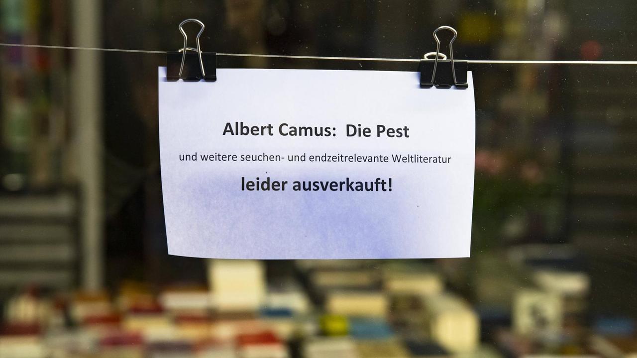 Auf einem Schild an einem Schaufenster einer Buchhandlung steht. Albert Camus - Die Pest und weitere seuchen- und endzeitrelevenate Weltliteratur leider ausverkauft! Auf einem Schild an einem Schaufenster einer Buchhandlung steht. Albert Camus - Die Pest und weitere seuchen- und endzeitrelevenate Weltliteratur leider ausverkauft!