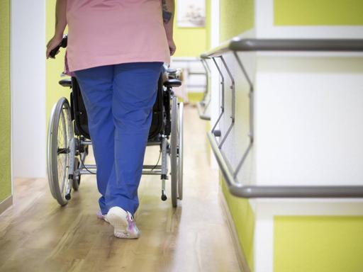 Eine Altenpflegerin schiebt eine Bewohnerin in einem Altenpflegeheim in einem Rollstuhl den Gang entlang.