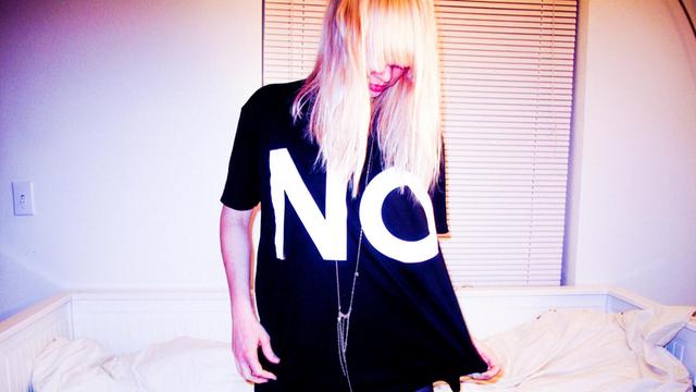 Musikerin EMA auf einem Bett, ihr T-Shirt verkündet ein großes "NO" (Bild: City Slang / EMA)