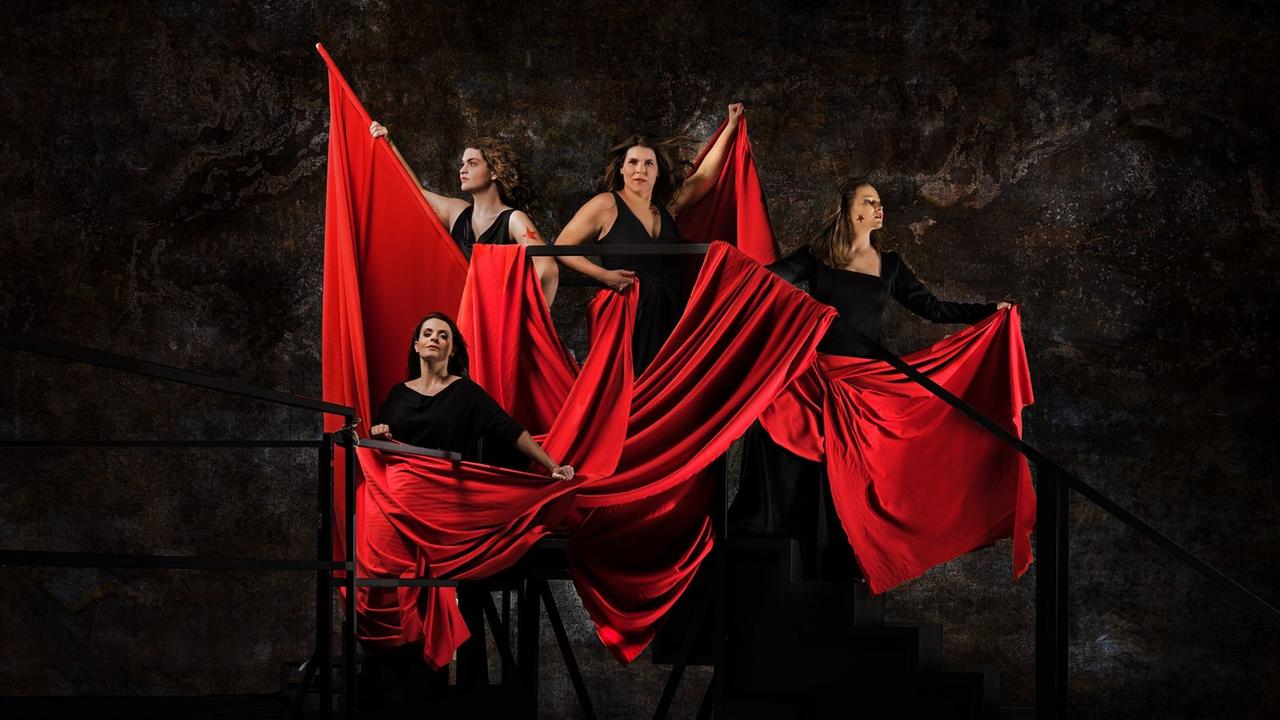 Vier Frauen stehen auf einem Gerüst, von einem großen roten Fahnentuch umgeben.