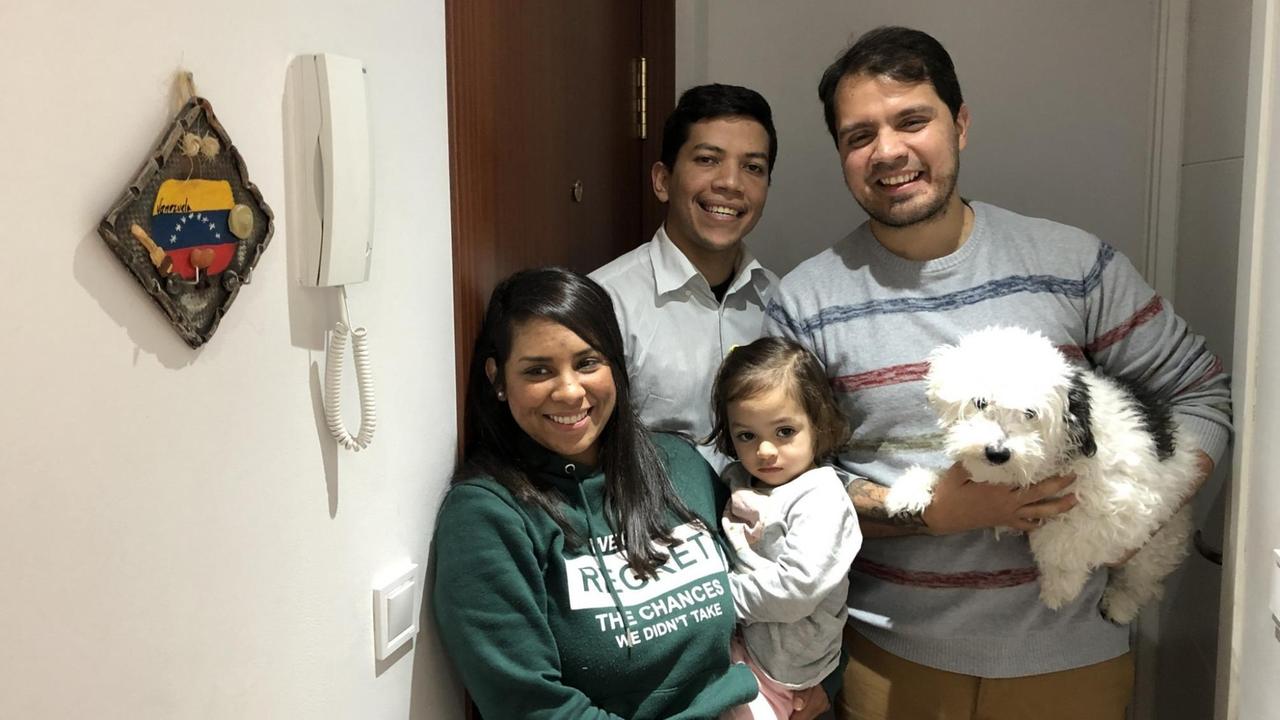 Carlos seine Frau Carolina mit ihrem Kind und ihr Freund Javier neben einem Schlüsselbrett mit Venezuelaflagge