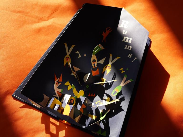 Das aufgeschlagene Kinderbuch "Eins, zwei, drei, die Akrobaten" auf orangenem Hintergrund.