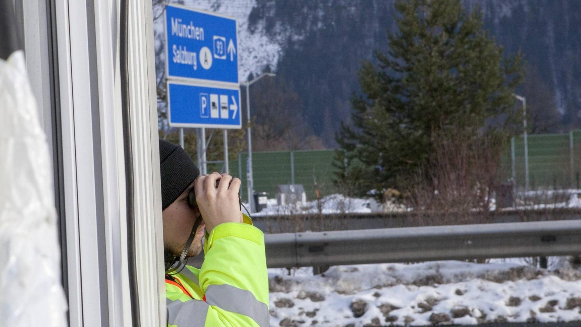 Ein Polizist steht an einer Autobahn und schaut durch ein Fernglas. Ein Polizist steht an einer Autobahn und schaut durch ein Fernglas.