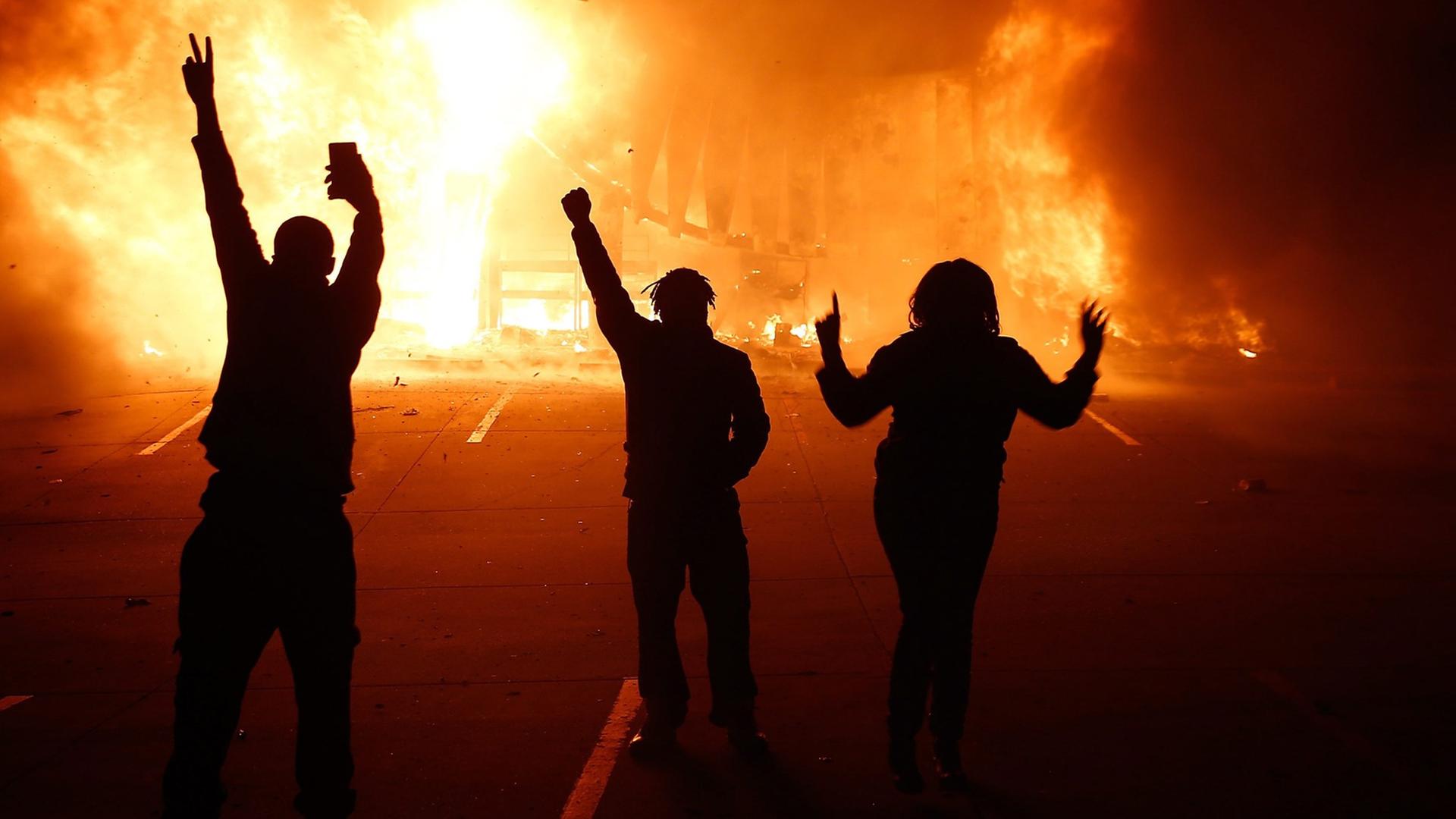 Krawalle in der Stadt Ferguson: Drei Protestierende jubeln in der Nacht vor einem brennenden Gebäude Krawalle in der Stadt Ferguson: Drei Protestierende jubeln in der Nacht vor einem brennenden Gebäude