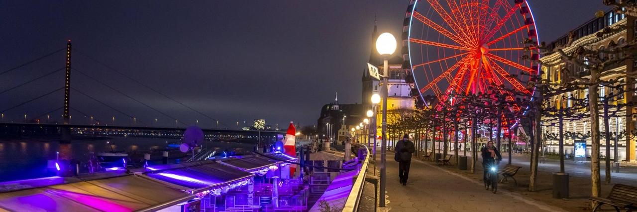 Blick auf die Düsseldorfer Altstadt mit Weihnachtsmarktständen, von denen viele geschlossen sind. Im Hintergrund ein rot leuchtendes Riesenrad. Blick auf die Düsseldorfer Altstadt mit Weihnachtsmarktständen, von denen viele geschlossen sind. Im Hintergrund ein rot leuchtendes Riesenrad.