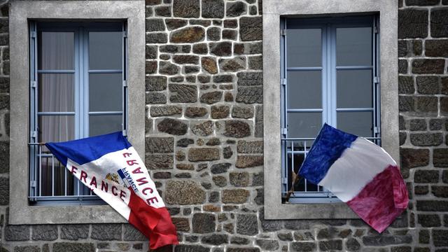 Zwei französische Fahnen hängen vor zwei Fenstern mit hellblauem Rahmen