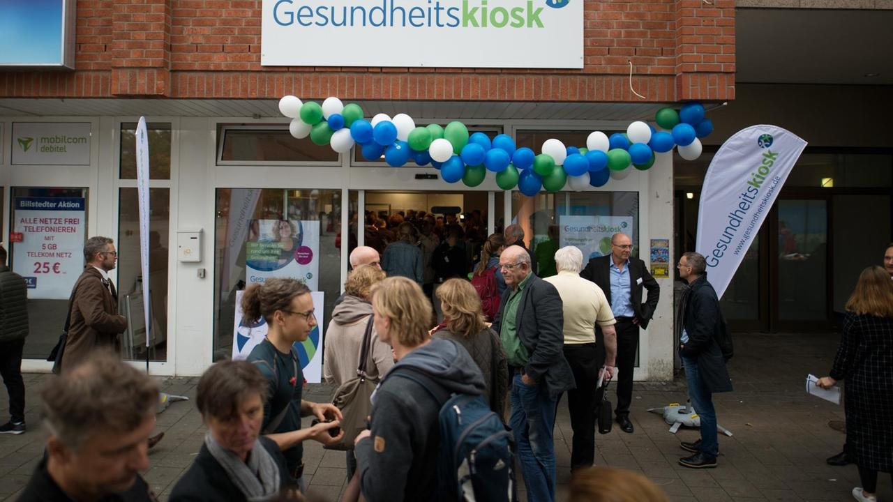 Passanten und Teilnehmer der Eröffnungsfeier stehen am 28.09.2017 vor dem neuen Gesundheitskiosk in Hamburg. In zentraler Lage wird das mehrsprachige Kiosk-Team aus Gesundheitsfachkräften die Bürger aus den Stadtteilen Billstedt und Horn kostenlos zu allen Fragen der Gesundheit beraten. Foto: Daniel Reinhardt/dpa | Verwendung weltweit Passanten und Teilnehmer der Eröffnungsfeier stehen am 28.09.2017 vor dem neuen Gesundheitskiosk in Hamburg. In zentraler Lage wird das mehrsprachige Kiosk-Team aus Gesundheitsfachkräften die Bürger aus den Stadtteilen Billstedt und Horn kostenlos zu allen Fragen der Gesundheit beraten. Foto: Daniel Reinhardt/dpa | Verwendung weltweit
