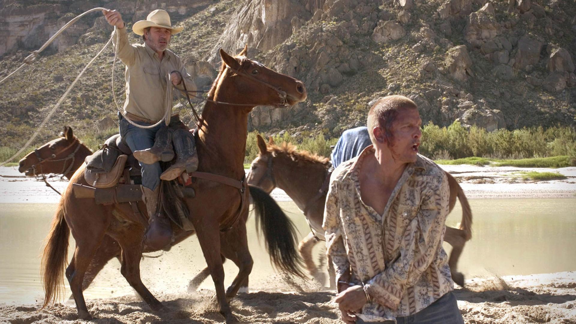 Filmszene aus Three Burials: Pete Perkins (l, gespielt von Tommy Lee Jones) versucht auf einem Pferd sitzend Mike Norton (Barry Pepper) mit einem Lasso zu fangen.