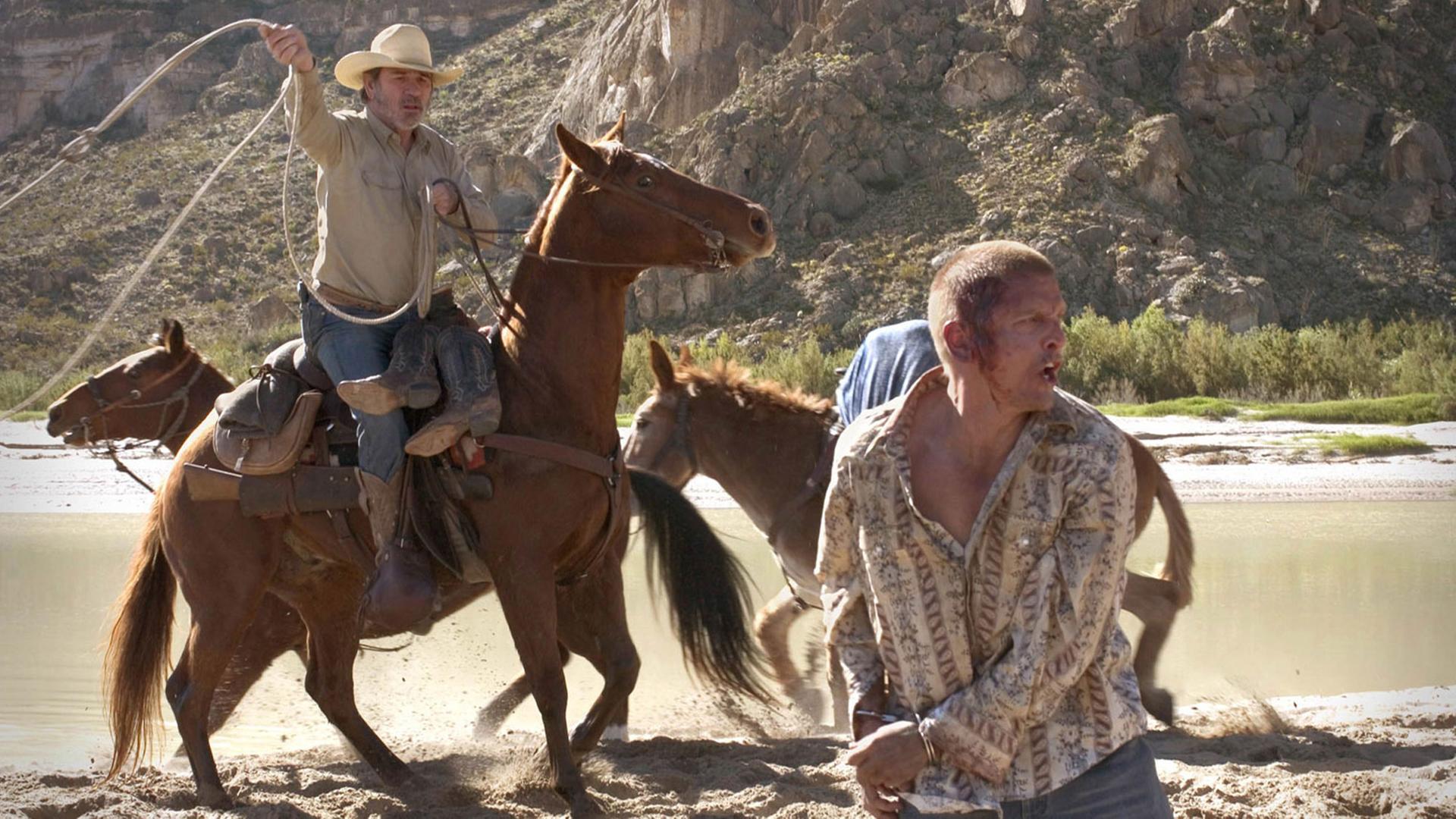 Filmszene aus Three Burials: Pete Perkins (l, gespielt von Tommy Lee Jones) versucht auf einem Pferd sitzend Mike Norton (Barry Pepper) mit einem Lasso zu fangen. Filmszene aus Three Burials: Pete Perkins (l, gespielt von Tommy Lee Jones) versucht auf einem Pferd sitzend Mike Norton (Barry Pepper) mit einem Lasso zu fangen.
