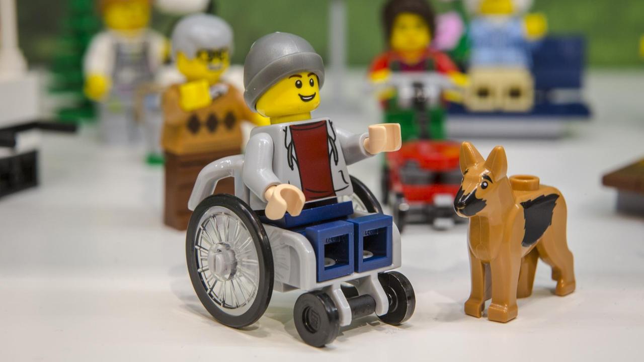 Man sieht eine Lego-Figur. Sie zeigt einen jungen Mann im Rollstuhl, der einen Hund als Assistenz hat.